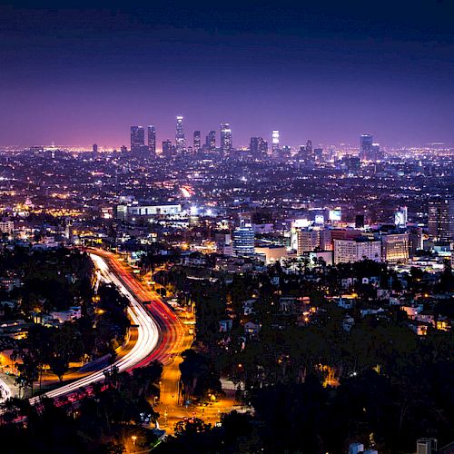 The image showcases a vibrant nighttime cityscape with illuminated buildings and a winding highway leading into the bustling urban center.
