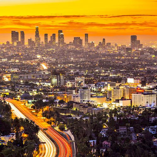 A stunning sunset view captures the vibrant cityscape of Los Angeles, with its iconic skyline and busy highways illuminated by city lights.