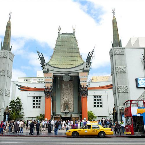 An ornate building with a pagoda-style roof, surrounded by tourists, a yellow taxi, and a double-decker bus in front.