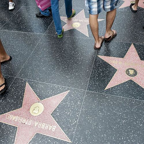 People walking on the Hollywood Walk of Fame, where Barbara Stanwyck's and Drew Barrymore's stars are visible on the ground.