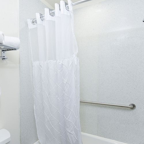 A bathroom with a shower/tub combo, white curtain, and rail, towels on a rack, and a showerhead.