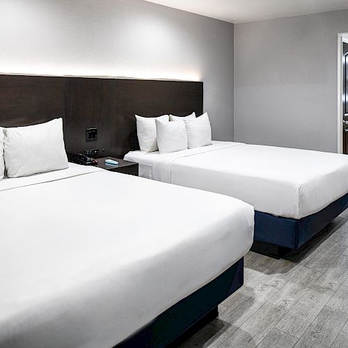 This image features a clean, modern hotel room with two neatly made double beds, a nightstand, and a view of an adjacent bathroom area.