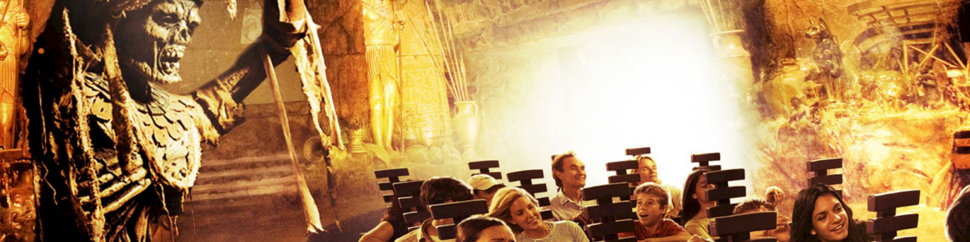 A group of people on an amusement park ride with an animated skeleton warrior wielding a sword in a haunted or ancient temple-themed setting.
