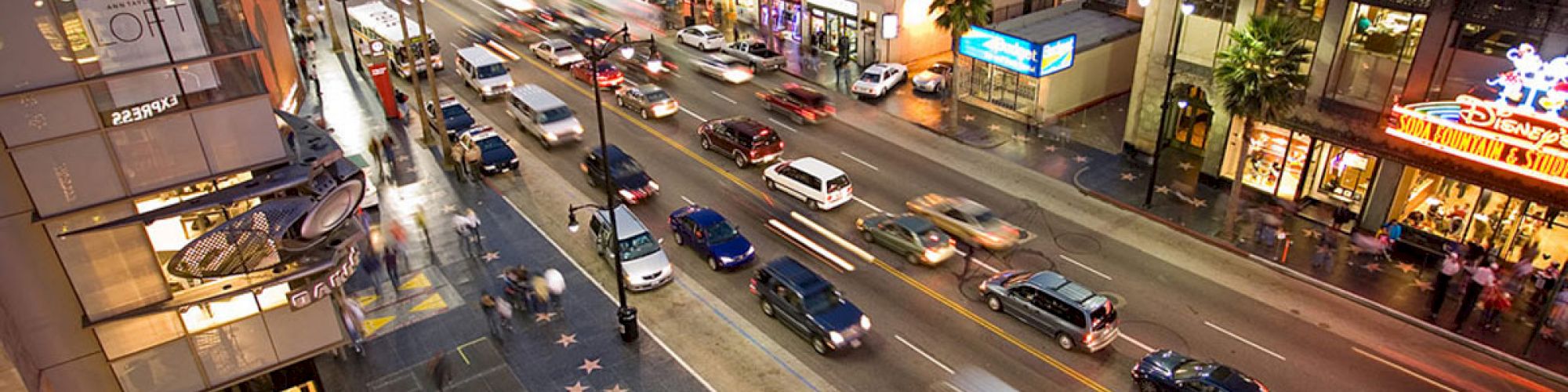 A lively city street scene with moving cars, busy sidewalks, and the star-studded Hollywood Walk of Fame visible on the pavement, ending the sentence.