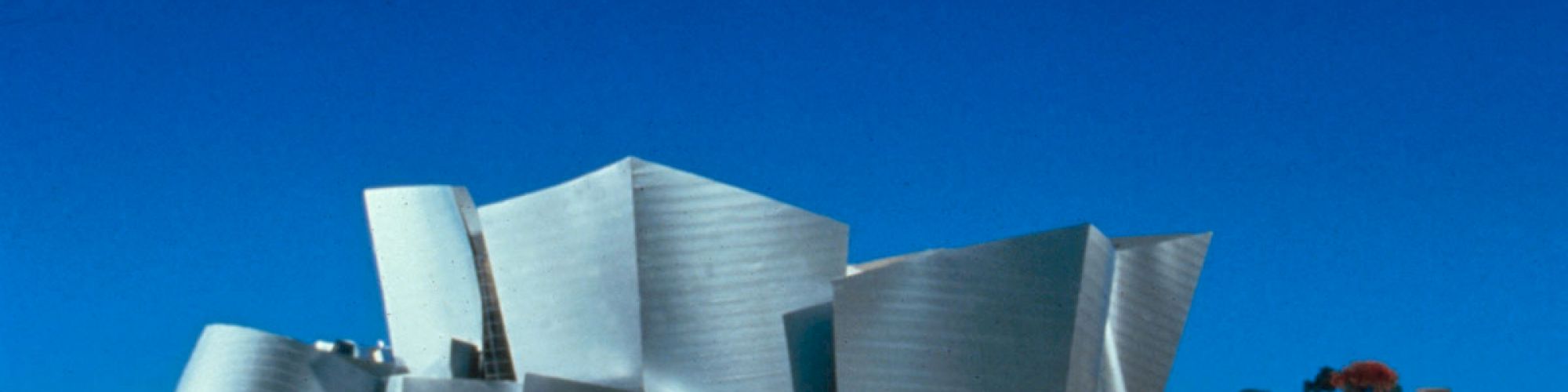 This image features a modern architectural building with metallic, angular, and irregular surfaces against a clear blue sky.