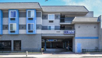 A modern inn with blue accents and an airplane flying overhead. The building has multiple windows and a covered garage area.