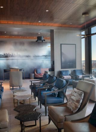 A modern lounge area with comfortable chairs, large windows with a waterfront view, and a wall mural of a city skyline.
