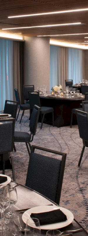 A modern, elegantly set dining hall with multiple round tables, each decorated with black tablecloths, white flowers, and neatly arranged tableware.