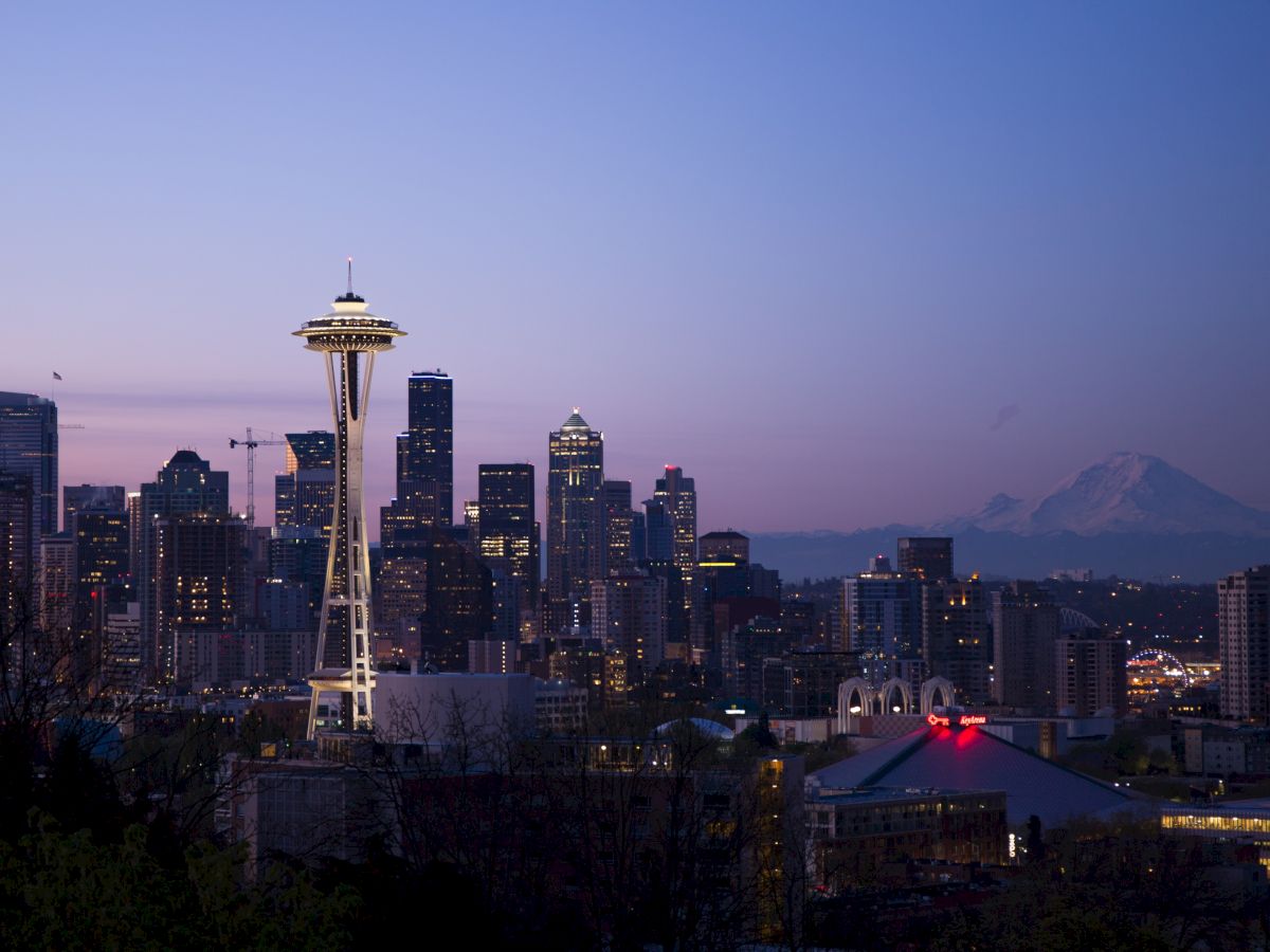 A twilight view of Seattle with its iconic Space Needle, modern skyscrapers, and Mount Rainier in the background.