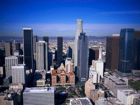 The image depicts a city skyline with numerous tall buildings, modern architecture, and a clear blue sky.