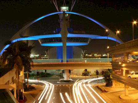 The image shows a nighttime view of a modern building with blue lighting and curving arches, surrounded by roads with streaks of car lights.