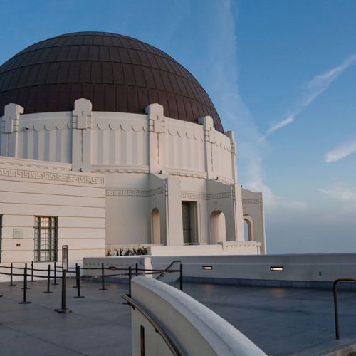 This image shows an observatory with a large dome and a white building structure under a blue sky with wispy clouds.